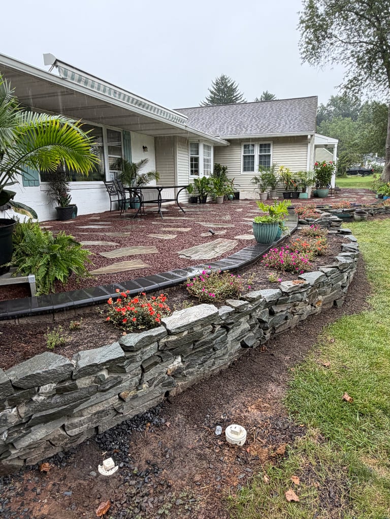 Single-story home with beige exterior, brick patio, decorative landscaping, stone retaining wall, and potted plants in front yard