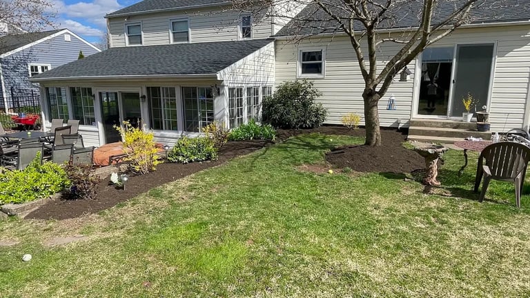 Suburban home with manicured lawn, garden beds, back patio, and seating area